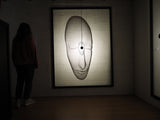 Arturo Álvarez illuminated mesh mask wall sculpture viewed by a person – handcrafted metallic mesh artwork casting a dramatic shadow on the wall